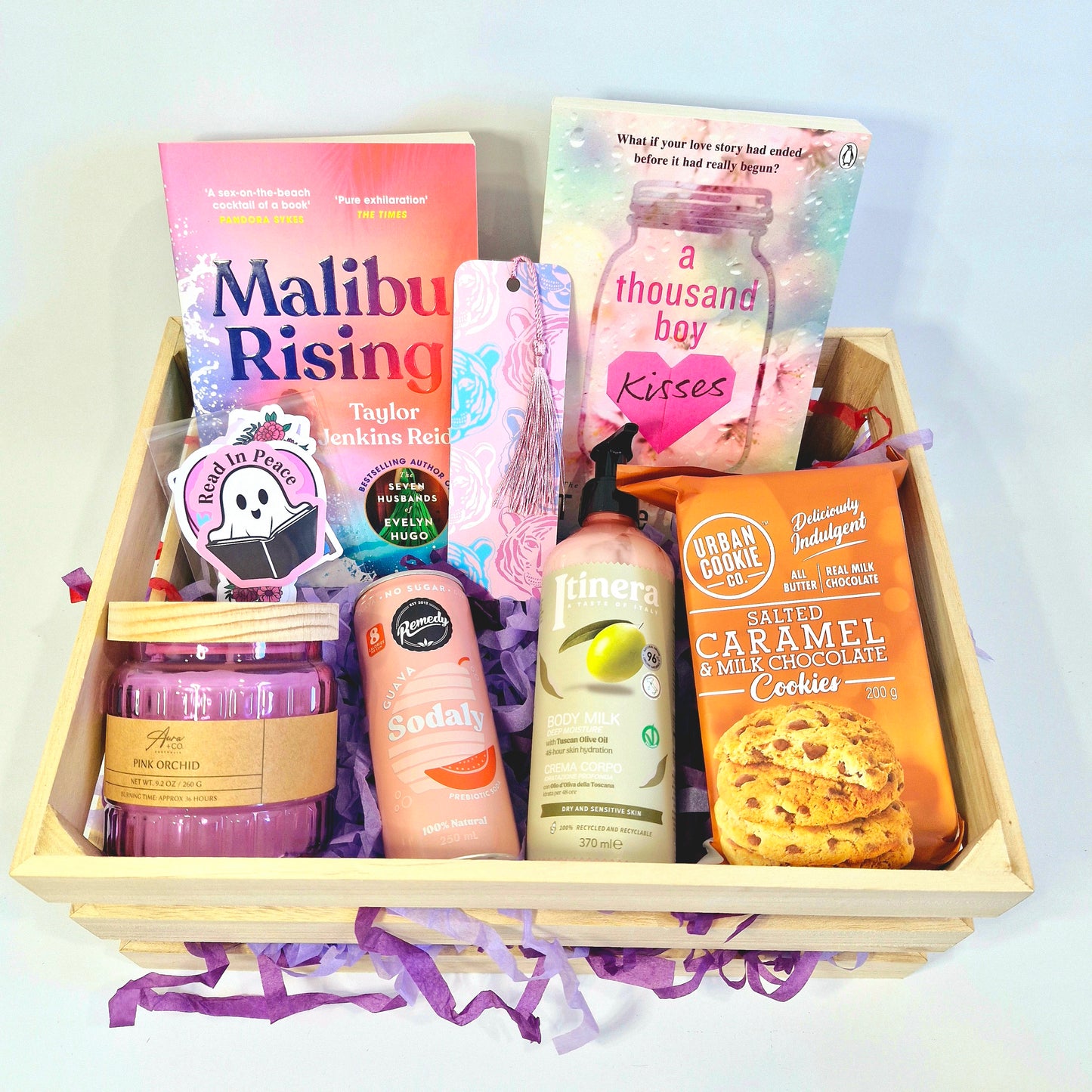 book gift box, reading subscription box containing paperbacks Malibu rising by Taylor Jenkins Reid and A Thousand Boy Kisses, candle, soda can, body lotion moisturiser, cookies, bookmark, stickers, bookish merch